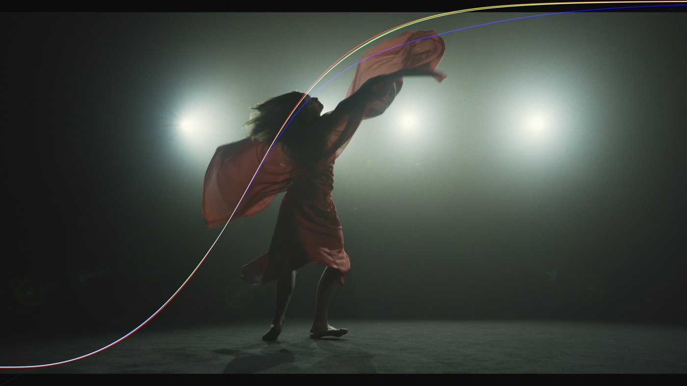 A backlit dancer with red, green, blue, and white characteristic curves crossing the frame.