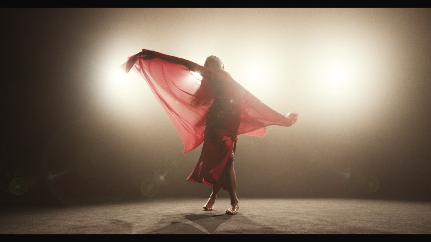 A dancer in a red dress swirls red fabric in front of bright stage lights and haze.